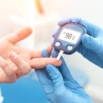 Healthcare professional in blue gloves checking a patient's blood glucose levels using a digital glucometer