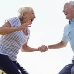 Happy senior couple holding hands and jumping with joy outdoors after receiving affordable medical treatment