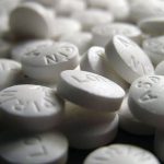 A close-up view of numerous white aspirin tablets scattered on a dark surface.
