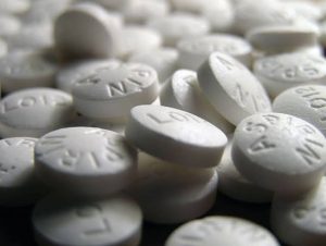 A close-up view of numerous white aspirin tablets scattered on a dark surface.