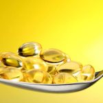 A metal spoon filled with translucent golden cod liver oil capsules.