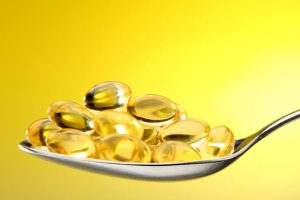A metal spoon filled with translucent golden cod liver oil capsules.