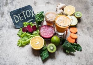 https://thecirclecaredoctors.com/shop/ A collection of fresh fruits and vegetables, including leafy greens, beets, citrus, and glasses of fresh juice, arranged on a surface with a "Detox" sign.