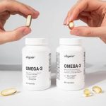 Hands holding golden Omega-3 softgel capsules above two white bottles of Omega-3 dietary supplements.