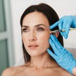 A clinical aesthetic procedure featuring a practitioner in blue gloves performing a facial PRP (platelet-rich plasma) injection on a patient to target fine lines and promote skin rejuvenation.