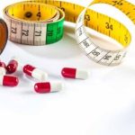 مجموعة متنوعة من الحبوب الطبية الملونة موضوعة على طبق بجانب شريط قياس أصفر، تعبيراً عن رحلة إنقاص الوزن والتحكم في الكتلة الجسمية.