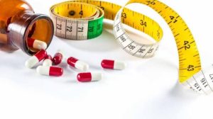 مجموعة متنوعة من الحبوب الطبية الملونة موضوعة على طبق بجانب شريط قياس أصفر، تعبيراً عن رحلة إنقاص الوزن والتحكم في الكتلة الجسمية.